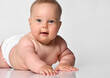 Close-up portrait of a six month old baby girl in a diaper lying and looking at you with interest on a white background