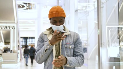 Wall Mural - Serious shopaholic in face mask walks along shopping mall and smartphone falls from guy hands and man catches device closeup