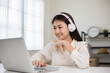 © Chanakon - Young asian woman in headphone using laptop chatting video conference online sitting in living room at home. Business Woman look at screen Meeting on social live steam. Work, learning from home.