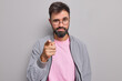 © WHstudio Leushin N - Self assured serious man with beard points index finger at camera chooses you looks directly at camera wears round spectacles casual jacket isolated over grey background. You should join my team