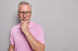 © wayhome.studio  - Horizontal shot of bearded thoughtful man holds chin looks pensively away being deep in thoughts has idea wears spectacles pink t shirt isolated over grey background copy space for your promotion