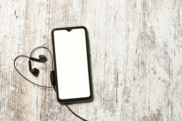 Wall Mural - mobile phone with empty screen and earphones on bright wooden background