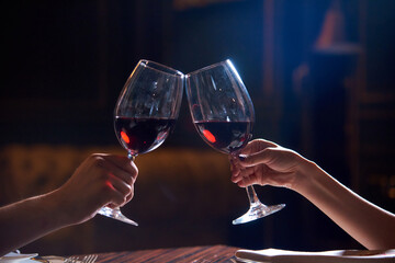 female and male hand holding glasses with red wine