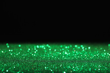 Wall Mural - shiny green glitter on black background, space for text. bokeh effect