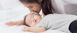 © NT_studio - Young asian mother kiss cheek of little baby girl with tender on bed in the bedroom, mom love newborn and care, mother with expression with child together, parent and daughter, family concept.