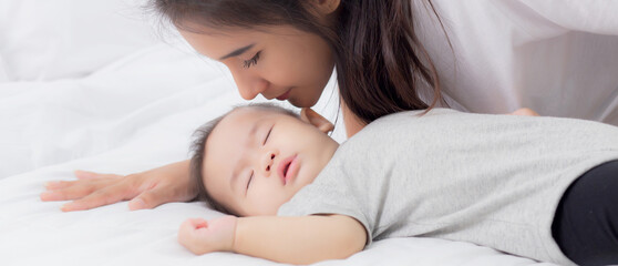 young asian mother kiss cheek of little baby girl with tender on bed in the bedroom, mom love newbor
