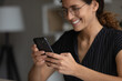 Close up smiling woman in glasses using smartphone, browsing mobile device apps, chatting with friends in social network, happy young female looking at screen, typing, writing message, scrolling
