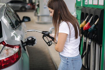 Wall Mural - Attractive young woman refueling car at gas station. Female filling diesel at gasoline fuel in car using a fuel nozzle. Petrol concept. Side view