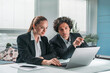 © ImageFlow - Businesswoman and businessman in formal suit are working together pensively looking into laptop display. Office background. Concept of teamwork