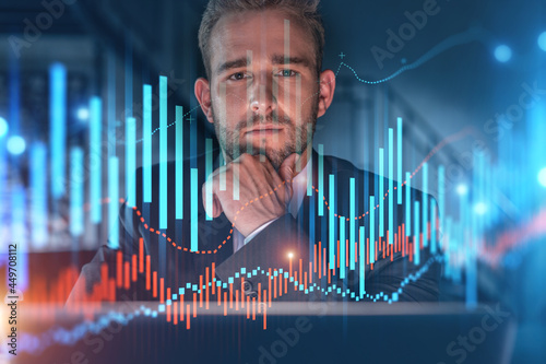 Portrait of handsome businessman in formal suit thinking how to optimize trading strategy at corporate finance fund. Forex chart hologram over modern office background. Hand on chin.