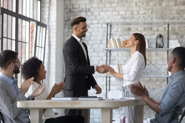 Happy young Caucasian businessman or boss shake hand of excited female colleague or partner close deal or agreement. Smiling male CEO handshake woman employee congratulate with promotion or success.