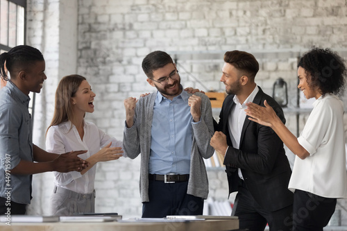 Smiling multiracial businesspeople congratulate colleague with job success or achievement. Happy supportive diverse multiethnic employees greet excited male worker with work promotion.