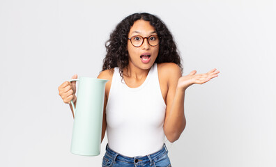 hispanic pretty woman feeling extremely shocked and surprised and holding a coffee thermos