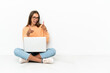 © luismolinero - Young woman with a laptop sitting on the floor pointing to the front and smiling