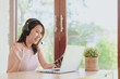 © interstid - Happy smiling Asian woman wearing headset having video conference via laptop at home in living room