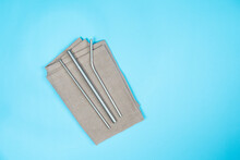 Metal Straws On Top Of A Brown Napkin In A Bluebackdrop. Metal Straws On A Wooden Plate In A Blue Backdrop. Save The Sea Animals And Reduce Plastic Usage! 