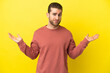 © luismolinero - Handsome blonde man over isolated yellow background having doubts while raising hands