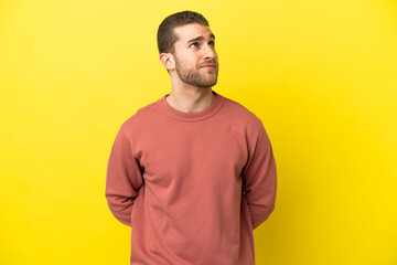 Handsome blonde man over isolated yellow background and looking up