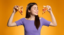 Happy Smiling Girl Holding Two Slices Of Pizza, Choosing What To Eat, Standing Against Orange Background. Concept Of Pizzeria Fast Food, Eating Out And Delivery