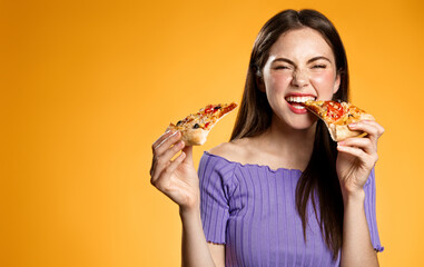 Image of brunette girl eating pizza with satisfaction, laughing, biting slices and looking pleased at camera, eat at pizzeria restaurant, orange background