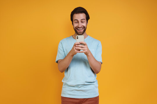 Portrait of excited young man in casual clothing looking at his smart phone and smiling