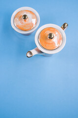 Poster - Top view of an orange covered teapot, a covered cup on a blue isolated background with free space