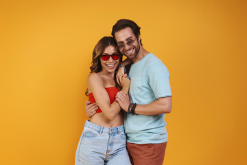 Poster - Beautiful young couple in eyeglasses embracing while standing against yellow background