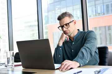 Wall Mural - Focused middle aged businessman corporate leader ceo executive manager thinking of online planning, business analyst analyzing financial market strategy using laptop computer sitting at office table.