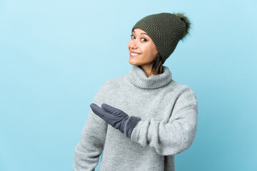 Wall Mural - Young Uruguayan girl with winter hat isolated on blue background extending hands to the side for inviting to come