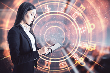 Poster - Attractive young european businesswoman using tablet with creative zodiac signs hologram on blurry background. Astrology concept. Double exposure.