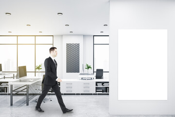 Poster - Businessman walking in bright coworking office interior with empty banner, window and city view, daylight, furniture and equipment. Mock up.