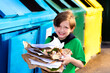 smiling european child standing at the trash can, boy is gooing to throw away sorted paper, saving the natural environment. metal trash for different garbage, an ecological approach