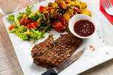Fototapeta Kuchnia - Traditional juicy grilled beef served with potatoes and vegetables in a cafe