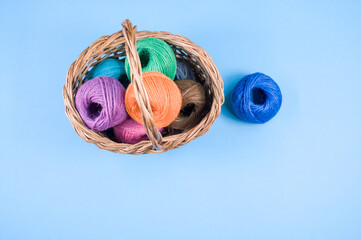 Poster - Pile of colorful textile balls of wool in a wicker basket on blue background with a copy space