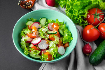 Wall Mural - Fresh vegetable salad in a ceramic bowl on gray background. Seasonal summer dish of tomatoes, cucumbers and radishes.