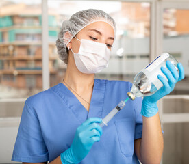 Wall Mural - Portrait of lady doctor with vial and syringe in her hands in professional protective clothing - medical mask and surgical cap