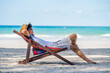 Asian man resting on beach chair at tropical beach. Happy guy sunbathing or nap on sunbed by the sea in sunny day. Young man relax and enjoy beach outdoor activity lifestyle on summer holiday vacation