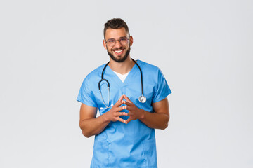 Wall Mural - Healthcare workers, medicine, covid-19 and self-quarantine concept. Friendly handsome doctor, nurse in blue scrubs and glasses with stethoscope, smiling, talking to patient during shift in hospital