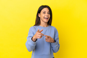 Poster - Young caucasian woman isolated on yellow background surprised and pointing front