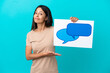 © luismolinero - Young woman over isolated background holding a placard with speech bubble icon and pointing it