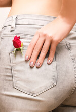 Red Rose In Woman Back Pocket. Female Buttocks In Gray Jeans With Red Rose Close Up. Female Hand With Peal Nail Design.