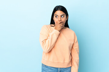 Wall Mural - Young latin woman woman isolated on blue background doing surprise gesture while looking to the side