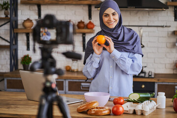 Wall Mural - Gorgeous Muslim woman holding an orange and talking to the camera with a smile