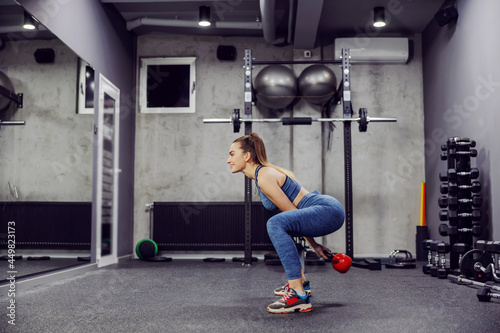 Swing exercise and dead lift dumbbells to burn the muscles of the buttocks and legs. A side view of a sexy woman in sportswear and in good physical shape lifting weights in an indoor gym