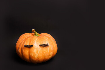 Pumpkin with false eyelashes on black background. Autumn, fall, halloween concept. copy space