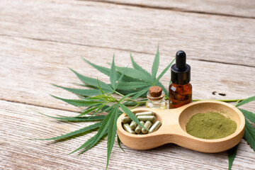 Wall Mural - Cannabis hemp essential oil and cbd powder capsule pill  with fresh organic marijuana plant isolated on wooden table background.