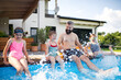 © Halfpoint - Father with three daughters outdoors in tha backyard, sitting by swimming pool.