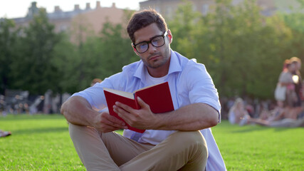 Young indian man reading book on green grass in park