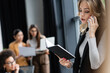 © LIGHTFIELD STUDIOS - young businesswoman looking in notebook while talking on cellphone near blurred multiethnic colleagues