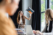 © LIGHTFIELD STUDIOS - excited businesswoman waving clipboard with charts while talking on smartphone near blurred colleagues
